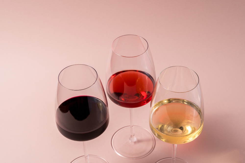Verre à vin rouge, verre à vin rose et verre à vin blanc sur fond rose.